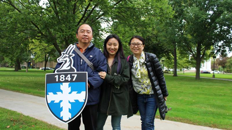 Student and parents pose for picture. Father is holding a LU crest shield