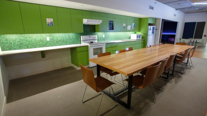 beige dining room and kitchen with lime green cabinets and backsplash. long wooden table in middle of room with wood and iron leg chairs