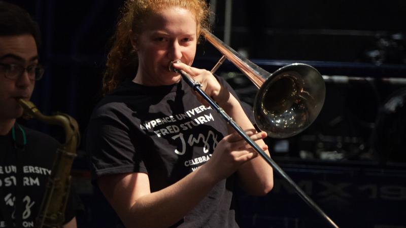 Woman plays trombone in stagelight on dark stage