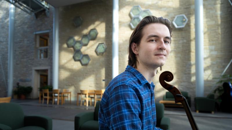 David Smith poses with his cello in the atrium that connects Steitz Hall of Science and Youngchild Hall of Science.