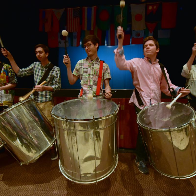 Drummers stand in a line playing large drums